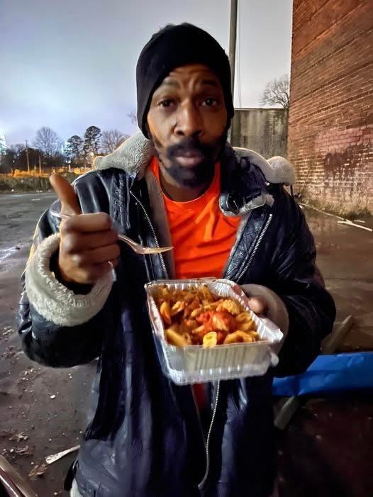 A man on the street holding an open container of hot food